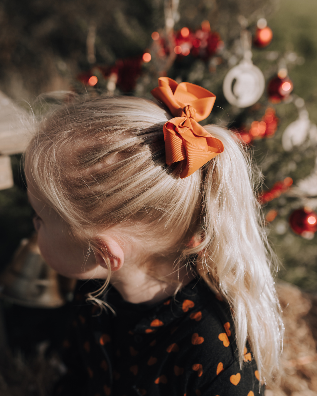Klein meisje met een extra grote haarstrik in het haar in de kleur bruin. De foto is gemaakt in een kerstsfeer.