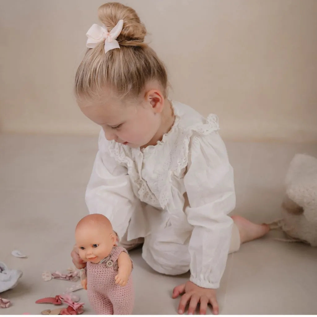 Kleutermeisje met grote strik in het haar speldend met pop en haarspeldjes
