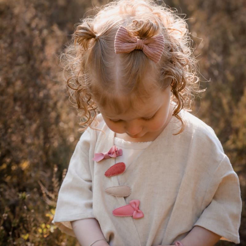Haaraccessoires, op de foto een meisje met een roze ribstof corduroy haarstrikje en haarspeldjes 