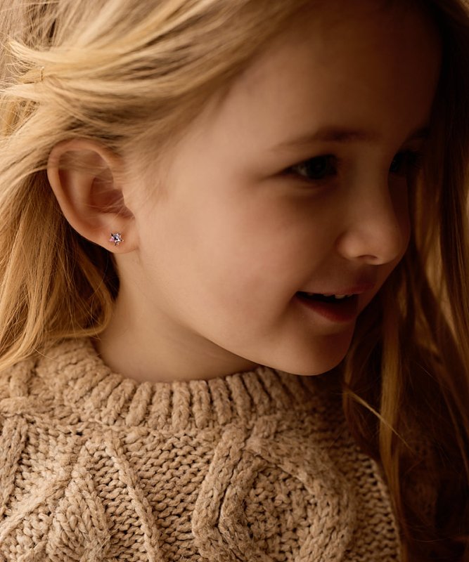 Meisje met een setje metaalvrije oorbellen van medical plastic in. Van het merk Blomdahl. De oorbelletjes zijn in de vorm van sterretjes en hebben de kleur paars.