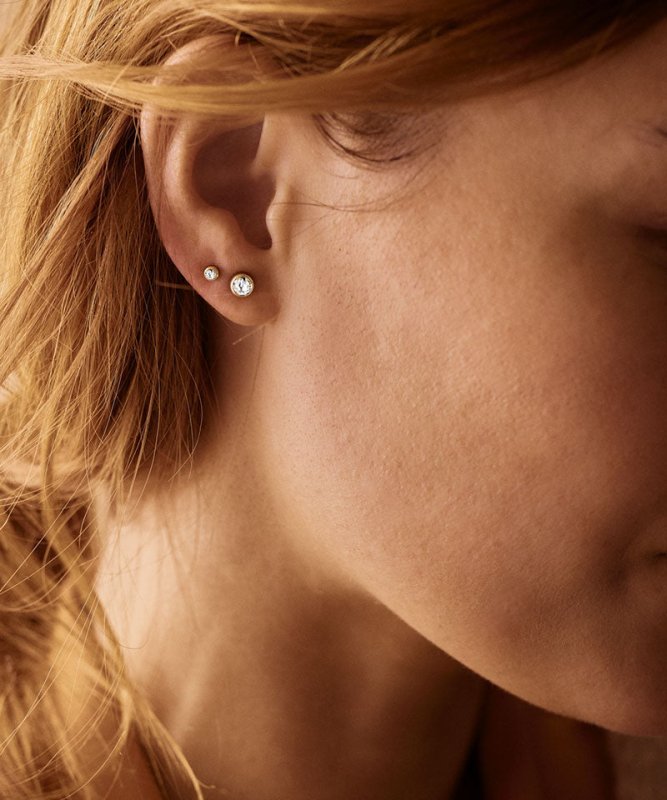 Een dame met 2 verschillende soorten maten goudkleurige titanium oorknopjes in. De titanium oorknopjes zijn van het merk Blomdahl.